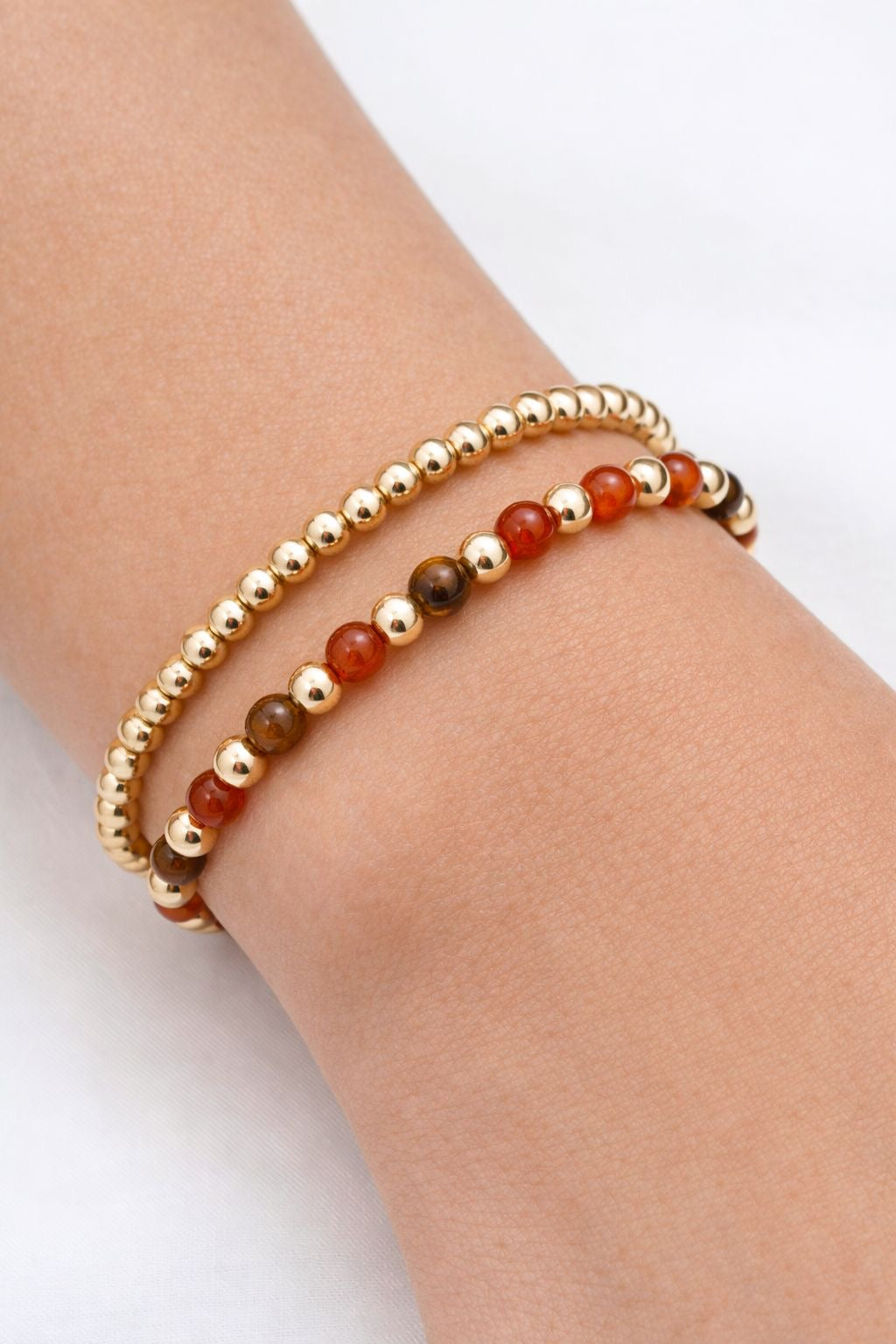 Bracelet with gold and red beads on a wrist against a white background
